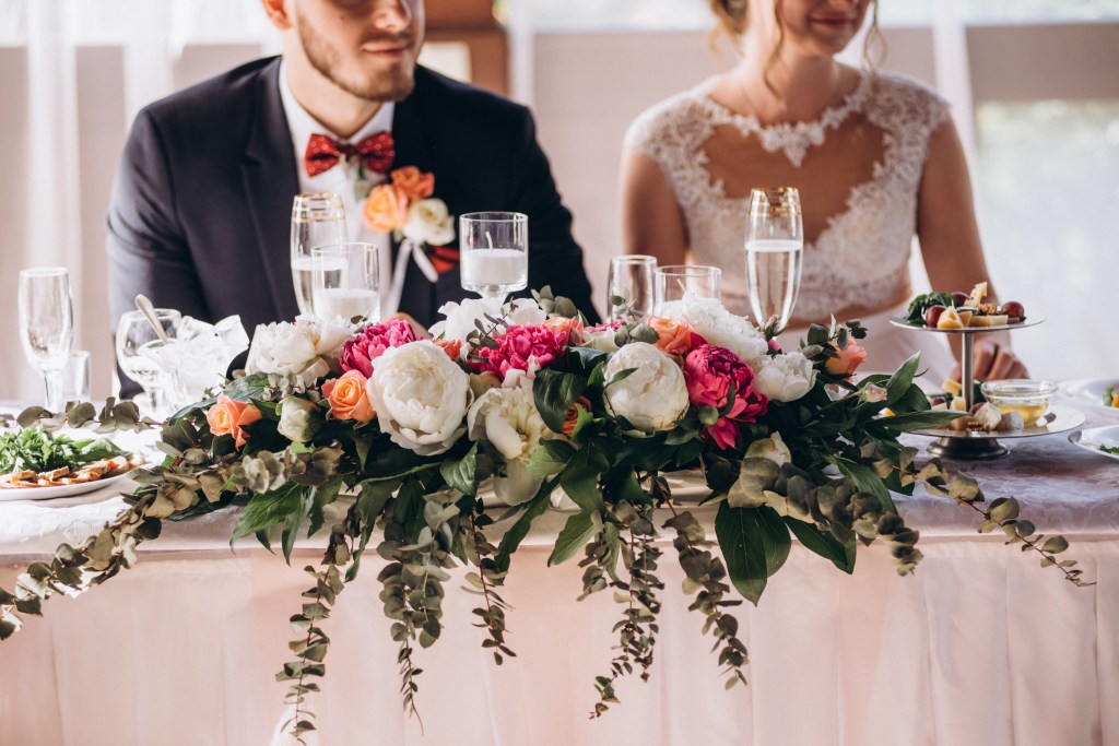 A wedding arrangement with beautiful colorful flowers on a table with a man and a woman sitting