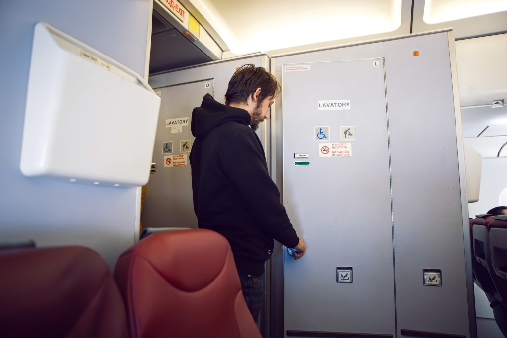 A hooded passenger lines up for the plane's bathroom.